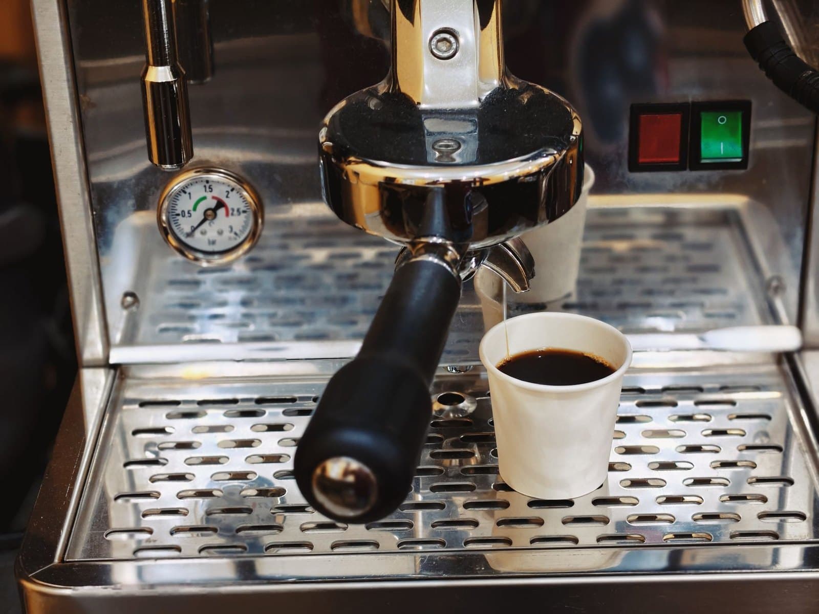 Espresso machine pouring into a cup with chrome group and portafilter in frame.
