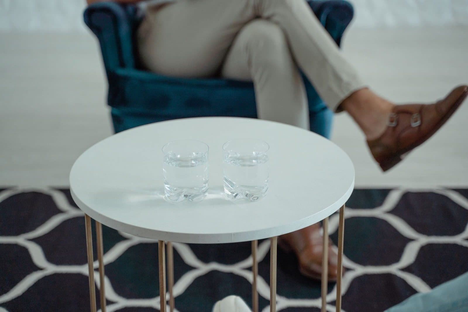 Two short clear glasses of water on a small round white table.