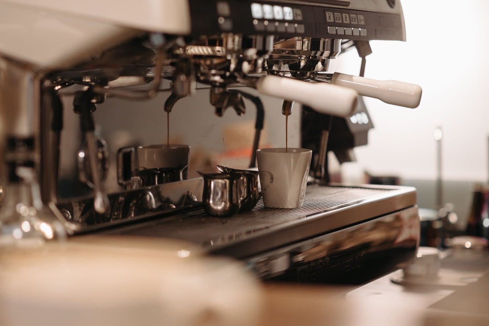 Chrome commercial espresso machine with portafilters locked in and espresso pouring into a white mug.