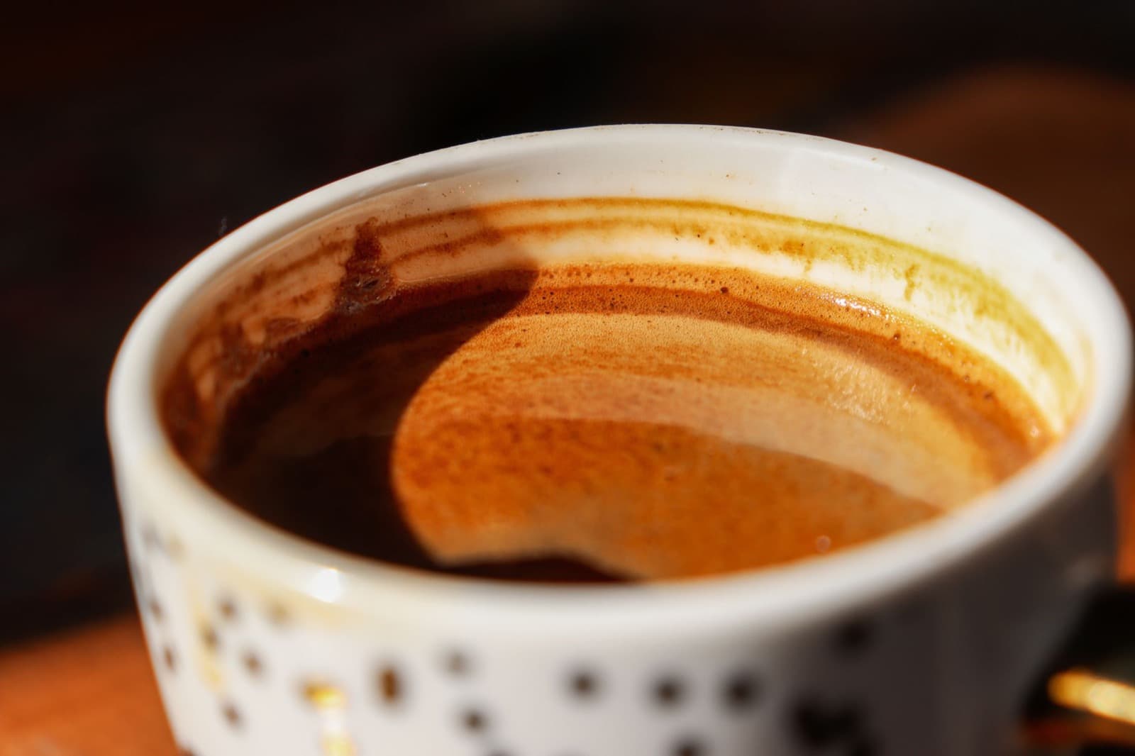 White dotted ceramic cup of espresso with thick golden-brown crema under side light.