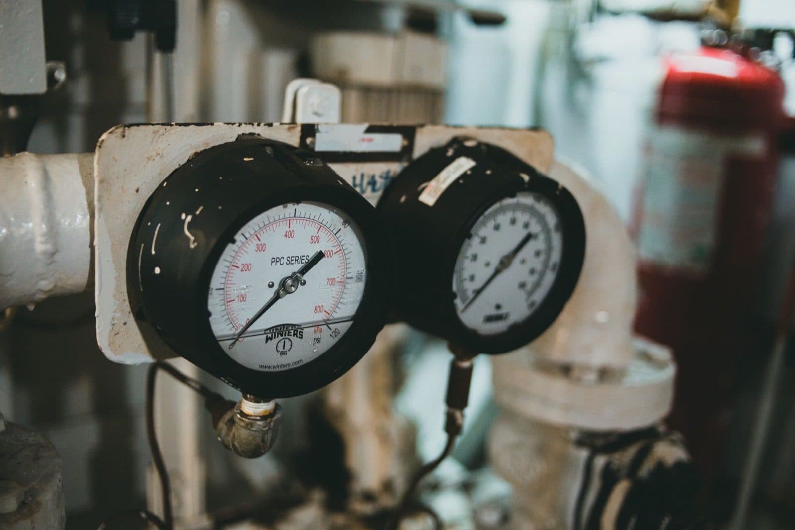 Two round industrial pressure gauges with black casings mounted on white piping.