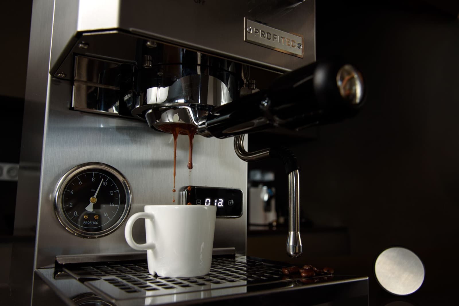 Profitec espresso machine extracting into a white cup beside an analog pressure gauge.