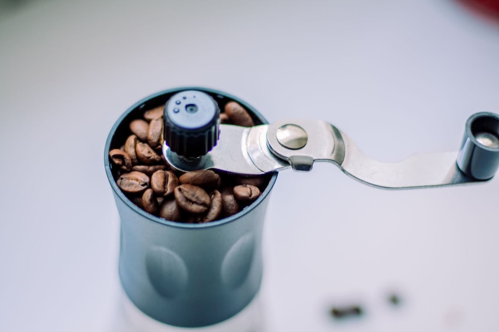 Manual hand grinder hopper filled with roasted coffee beans and a silver crank arm.