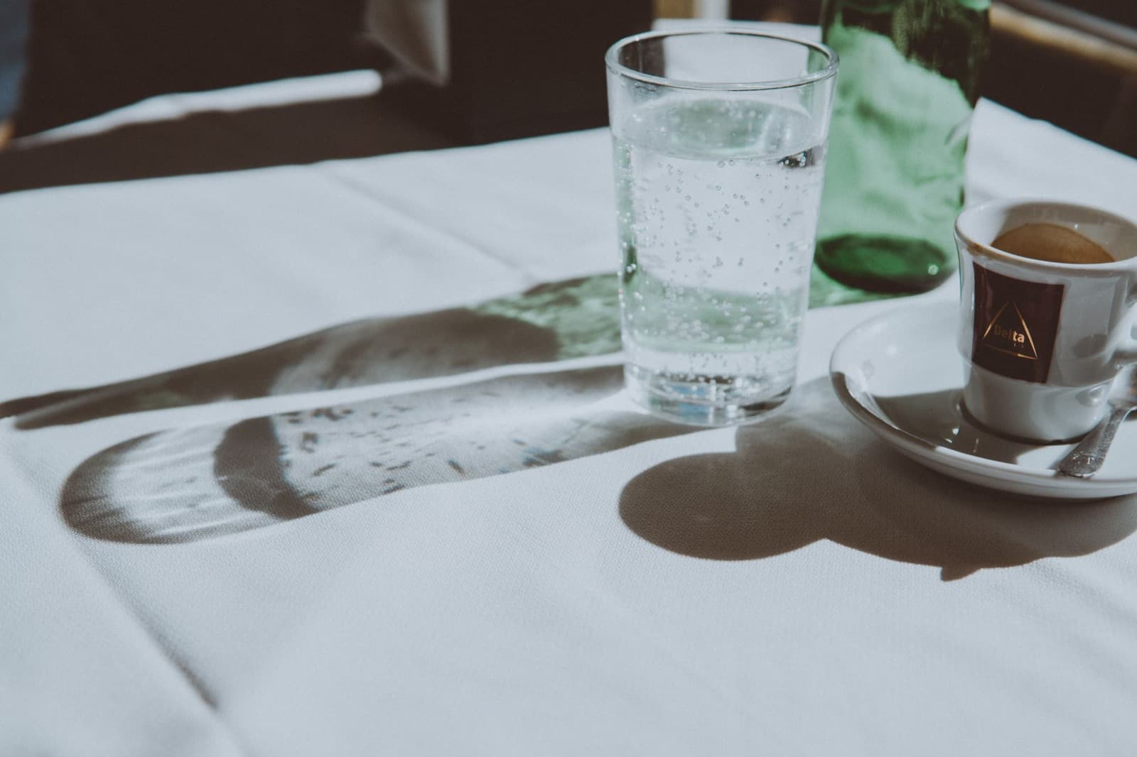Tall glass of sparkling water beside a small white espresso cup on a white tablecloth.
